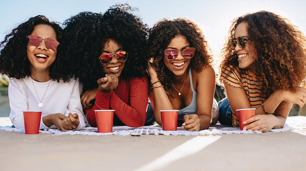 Four women with coily hair drinking coffee on the beach
