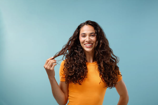 woman with wavy hair touching strands in blue background