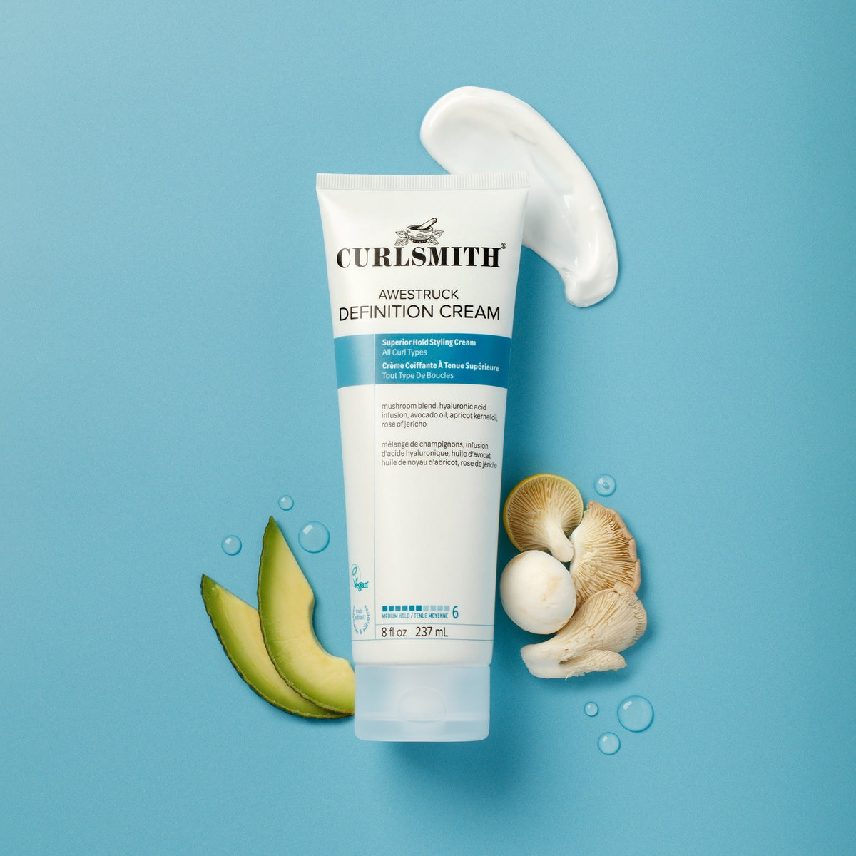Curlsmith Definition Cream tube with avocado and shell on a blue background