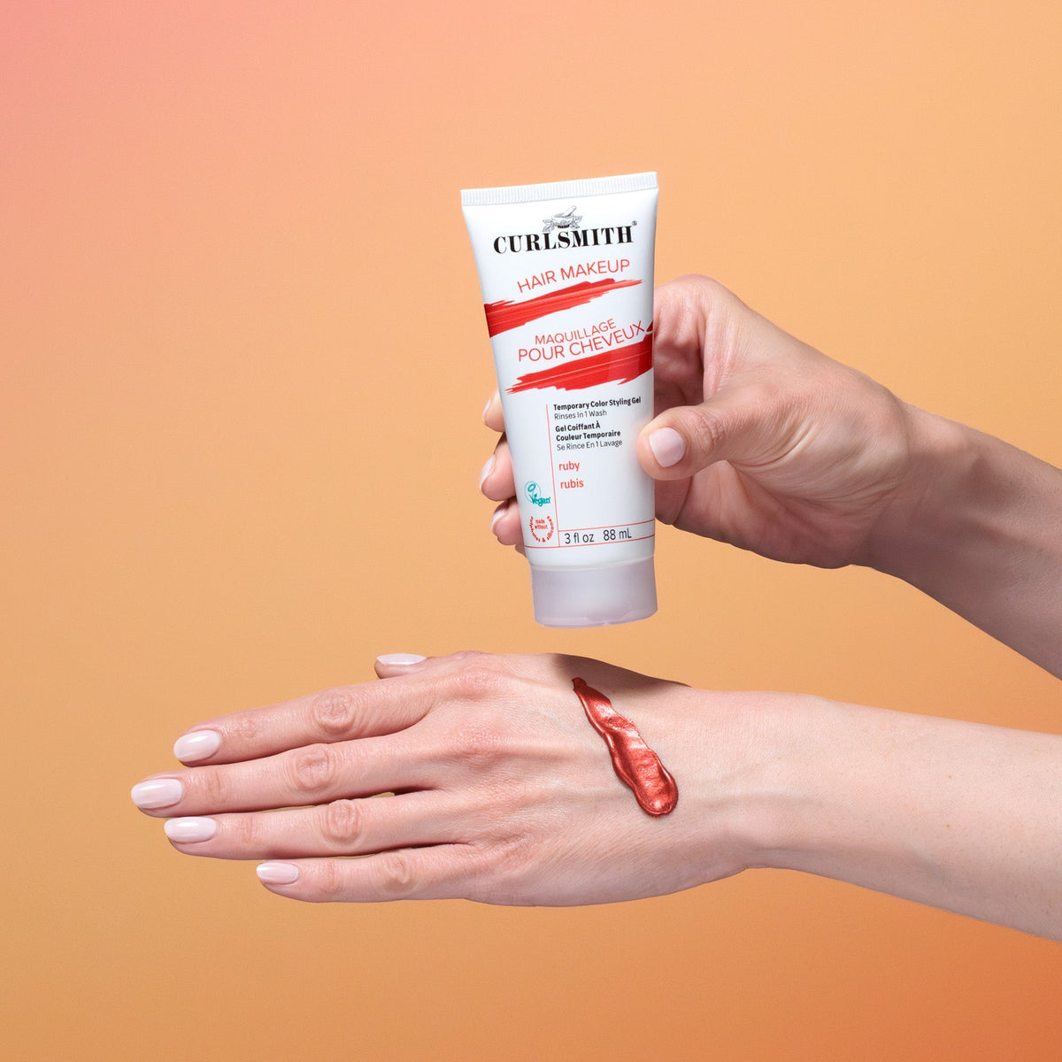 Hand holding a tube of Curlsmith hair makeup against an orange background