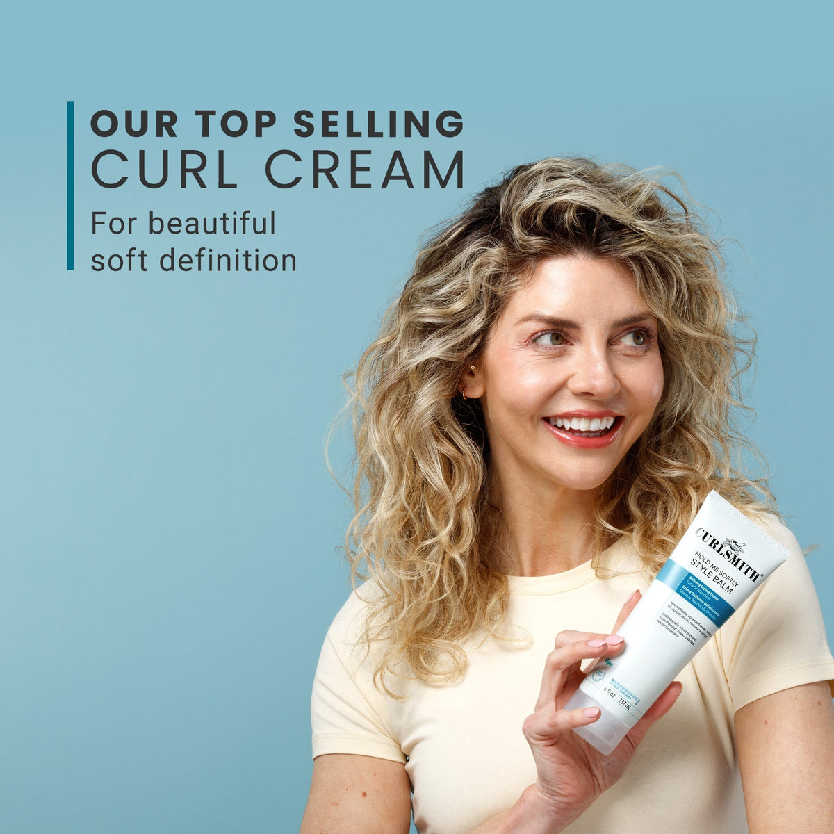 Woman holding a bottle of Curlyra curl cream against a blue background