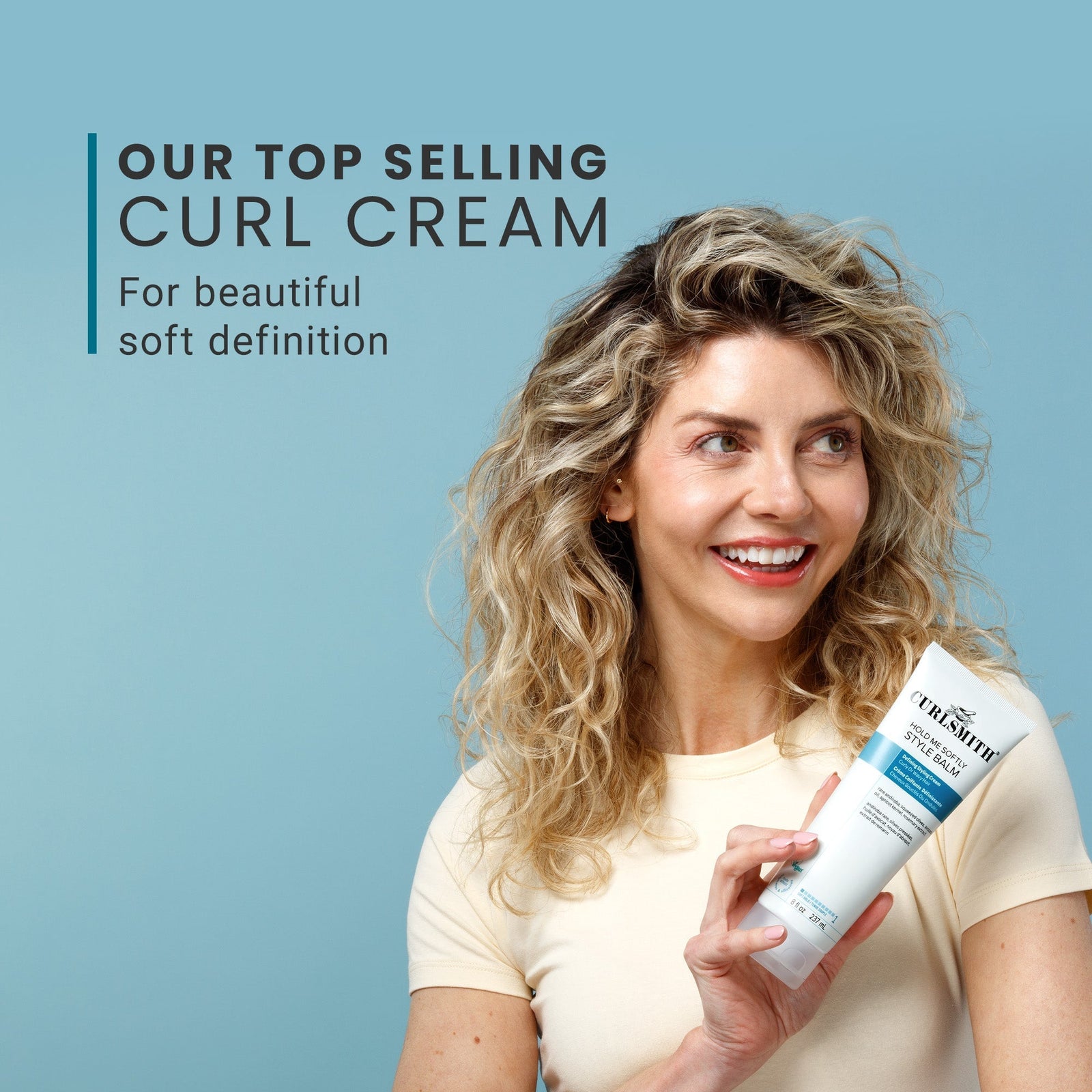 Woman holding a bottle of Curlyra curl cream against a blue background