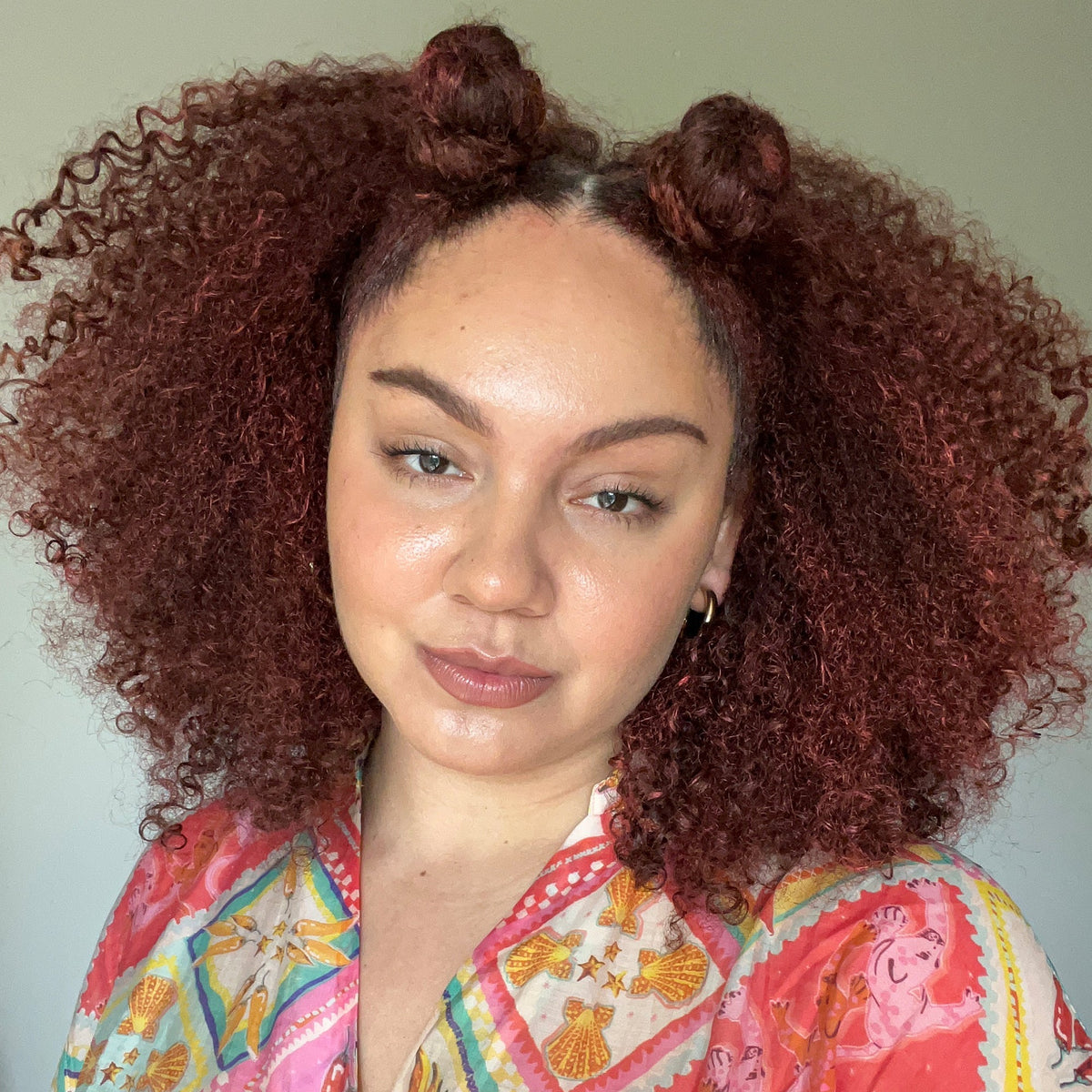 Woman with curly hair styled in buns wearing a colorful patterned top.